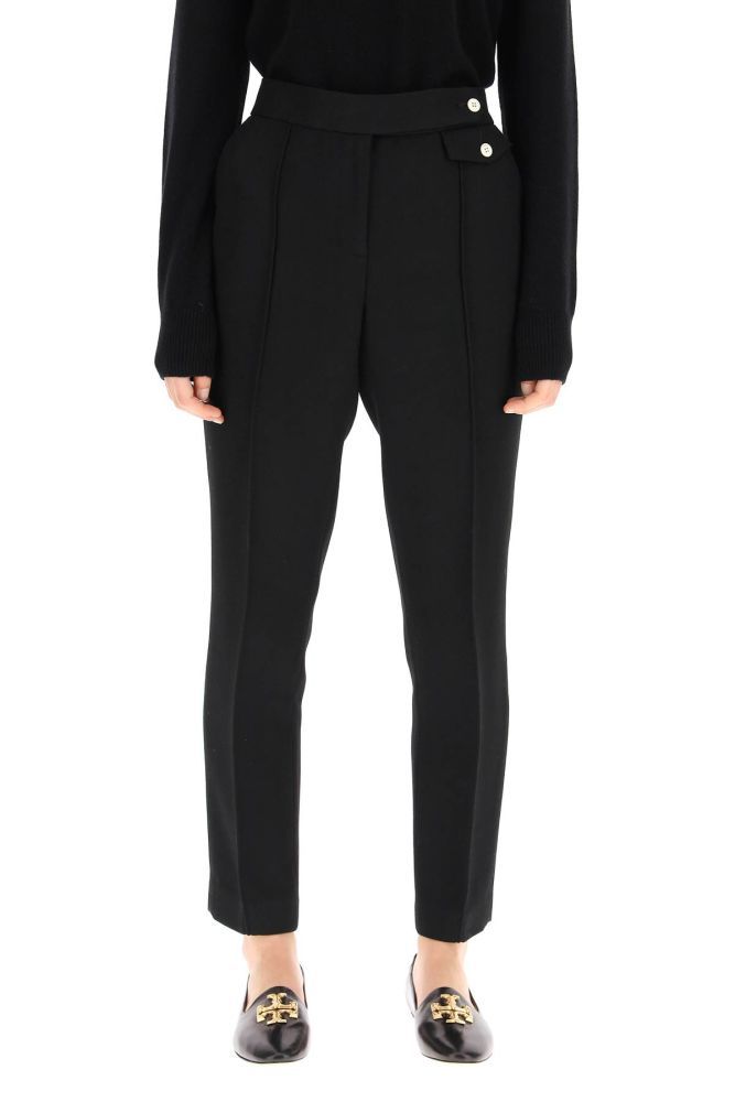 Tory Burch trousers crafted in woven fabric with a regular straight-leg cut. They feature central pintucks, concealed zip and hook closure, side slash pockets, rear welt pockets, small front pockets with buttoned flap. The model is 177 cm tall and wears a size US 4.