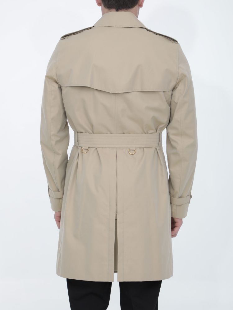 Kensington Heritage trench coat in beige cotton gabardine with double-breasted closure and adjustable belt on waist. It features epaulettes, hook-and-eye collar closure, two side buttoned welt pockets and belted cuffs. The model is 184cm tall and wears size 48.