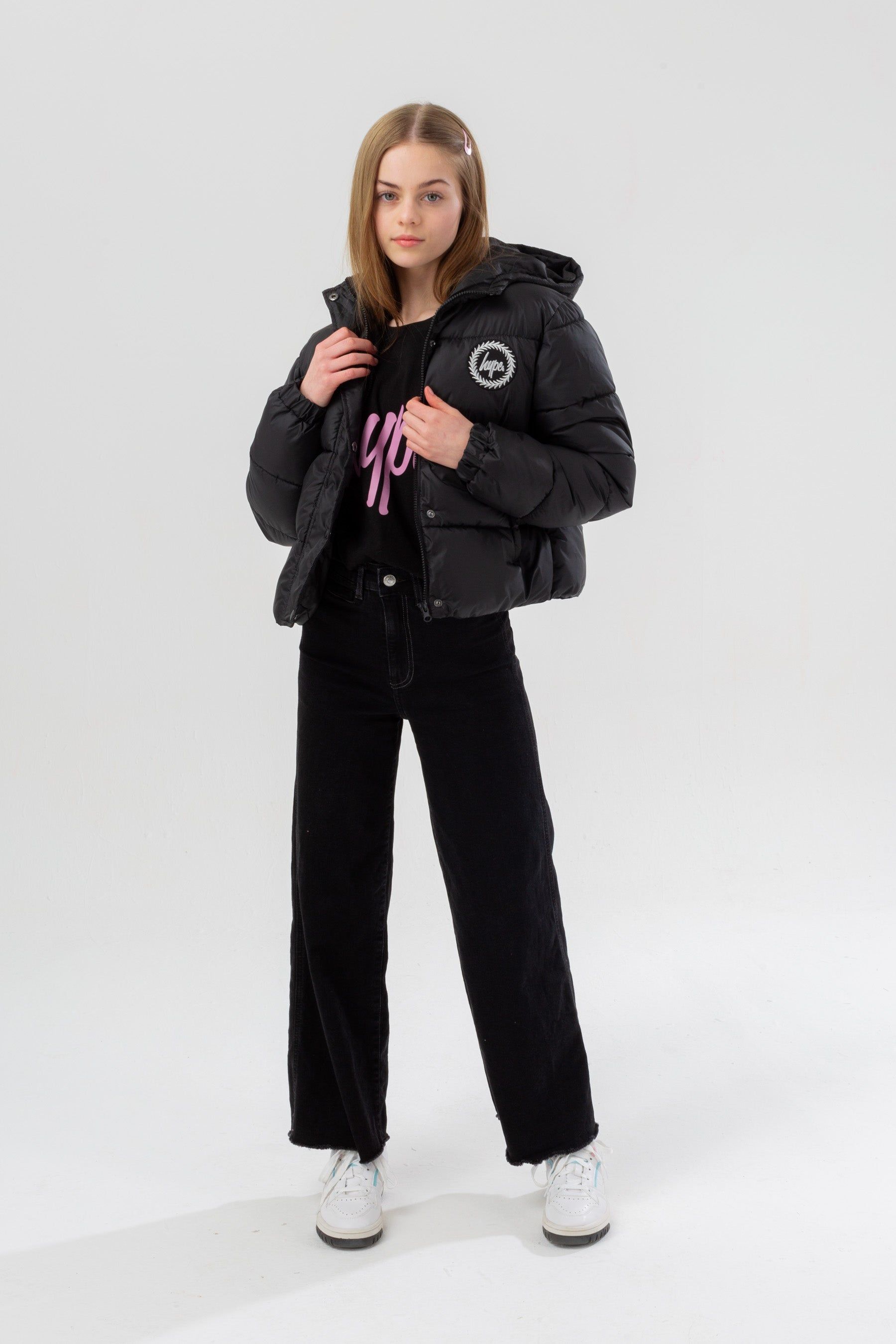 Meet the HYPE. Girls Black Cropped Kids Puffer Jacket, part of the HYPE. 2022 Back to School collection. The coat is designed in our standard cropped puffer shape in a classic black. Finished with padding, the iconic HYPE. crest badge logo in a contrasting monochrome, and two zip pockets on the front. Machine washable.