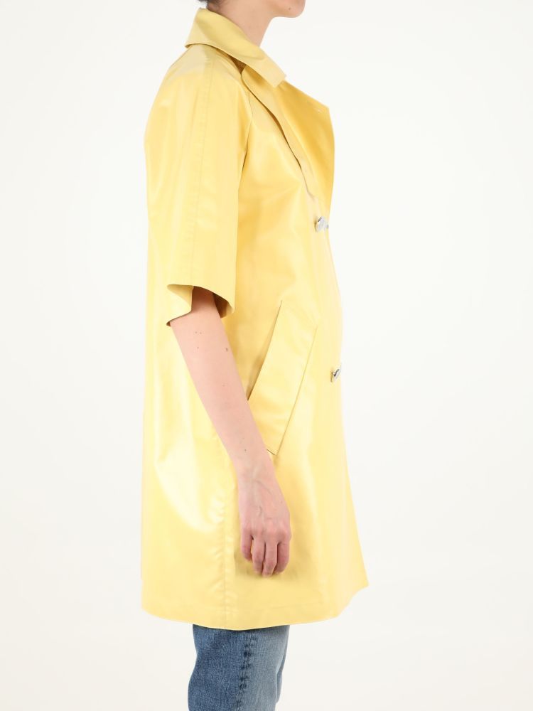 Short-sleeved yellow raincoat with double-breasted closure. It features two side maxi welt pockets and rear slit. The model is 180cm tall and wears size 38.