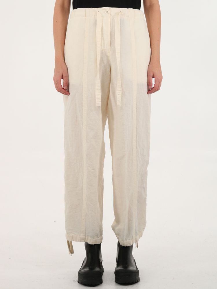 Crinkle-effect white trousers with relaxed fit and drawstring at the waist. They feature regular waist, wide leg, hidden button closure, side-seam pockets, back patch pocket, wide seam details and drawstring at hems. The model is 180cm tall and wears size 34 DE.  