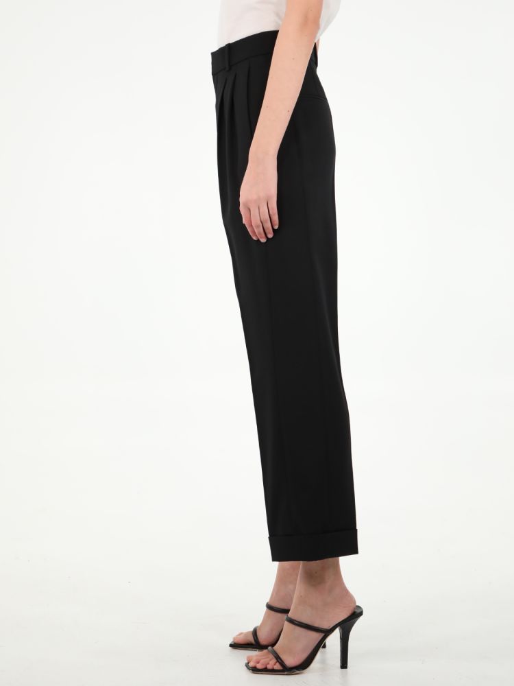 High-waisted wide-leg black trousers in grain de poudre. It features concealed button, hook and zip closure, two side slash pockets, center pleats, two rear welt pockets, upturned hems and belt loops. The model is 180cm tall and wears size 36.  