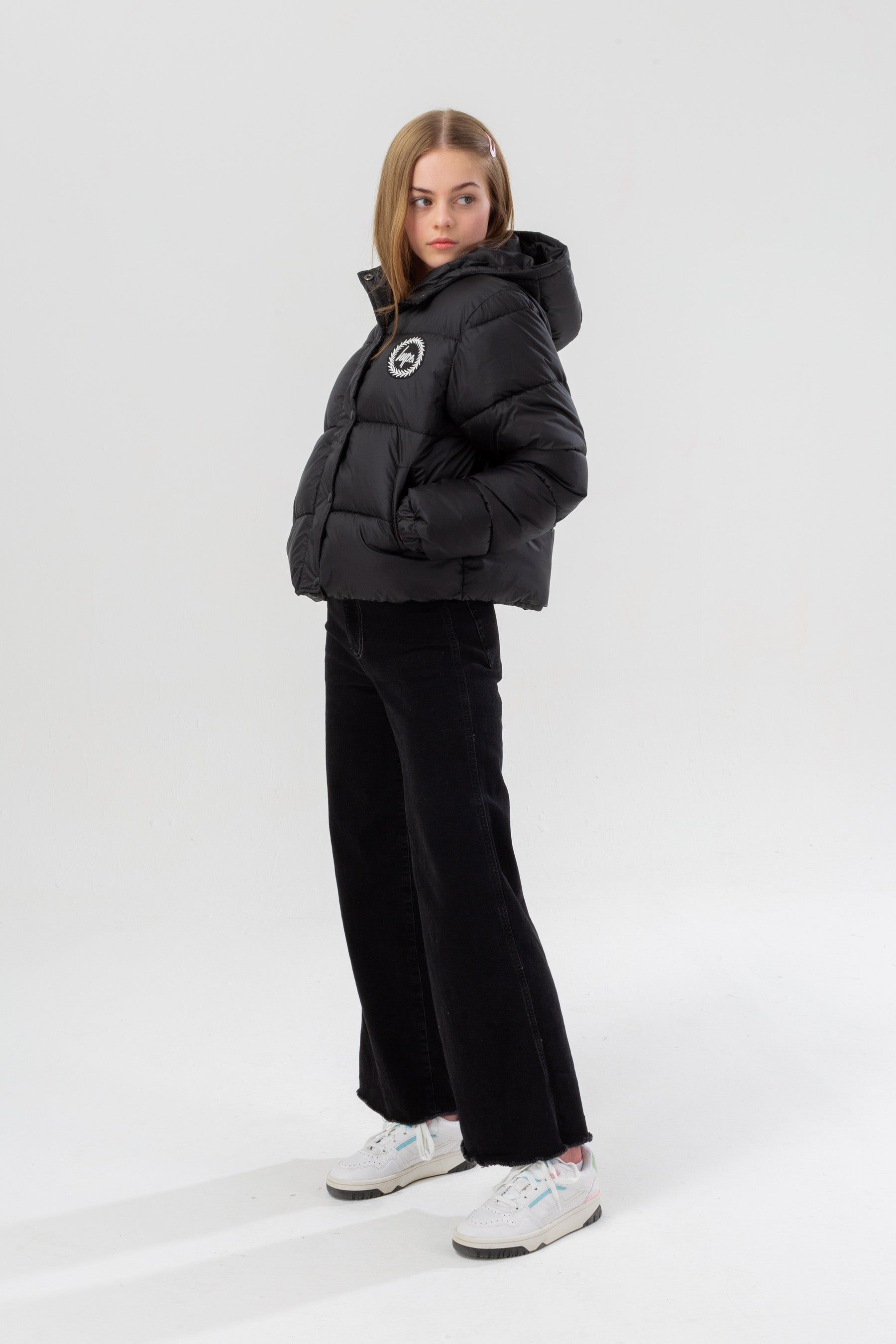 Meet the HYPE. Girls Black Cropped Kids Puffer Jacket, part of the HYPE. 2022 Back to School collection. The coat is designed in our standard cropped puffer shape in a classic black. Finished with padding, the iconic HYPE. crest badge logo in a contrasting monochrome, and two zip pockets on the front. Machine washable.