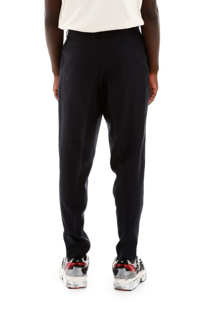 Etudes wool tailoring trousers with pressed pleats. Concealed zip and hook closure, front slanted pockets, back welt pockets. Metallic logo on the front. Model height is 183 cm and he is wearing a size IT 46.