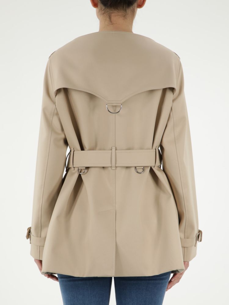 Short beige cotton raincoat with double-breasted closure. It features front buttons, adjustable belt on waist, two side buttoned welt pockets, adjustable buckle on cuffs and back slit.The model is 178cm tall and wears size 6.