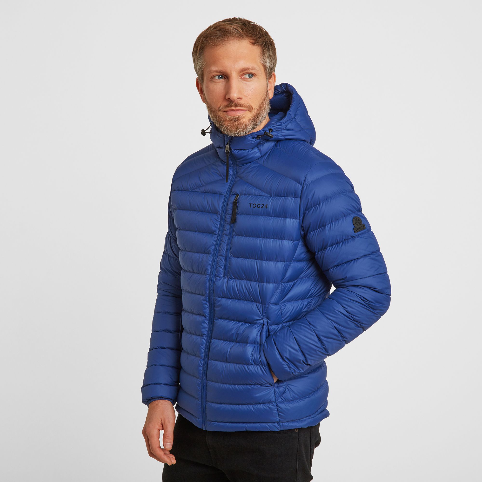 Perfect for adding a layer of warmth without any bulk, our Drax down filled mens jacket with adjustable hood feels silky-soft, incredibly light and packs down small into a zip up inside pocket. You'll have no trouble finding room for it in your case when you go away, and it also makes a handy travel pillow. This padded jacket gets its incredible warmth from naturally insulating duck down that traps heat without being bulky. Quilted bands, a panelled cut and a hood that hugs your neck mean it feels as good as it looks, and it has thoughtful details like a soft chin cover over the top of the zip. Designed to squish down really small, then spring back into shape, Drax has roomy side pockets protected by an elasticated flap, light elastic at the cuffs and small toggle adjusters at the hem keep the chill out.  Designed in Yorkshire, where we always need layers, our Drax mens hooded jacket is ideal for wearing over a top when it's only a bit chilly or layering under a coat when the wind is howling. Reflecting our Spen Valley ethos of Truth Over Glory, it has a TOG24 logo proudly printed on the chest.