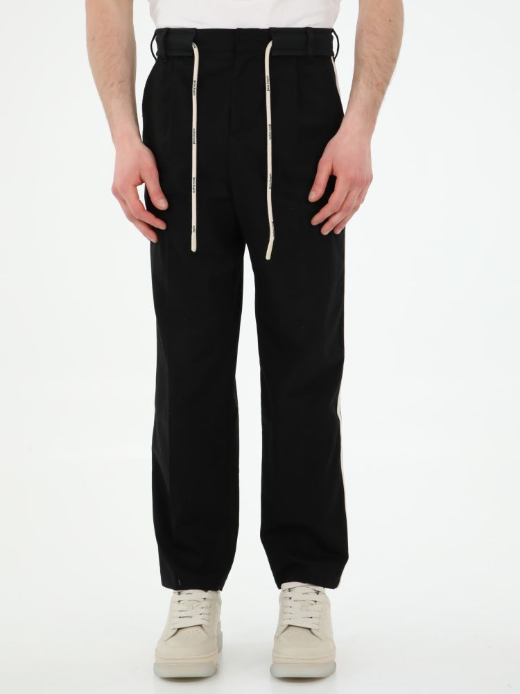 Black track pants with tone-on-tone belt and white drawstring with Palm Angels logo. It features white side stripes, two side welt pockets, two rear buttoned welt pockets and belt loops. The model is 184cm tall and wears size 48.
