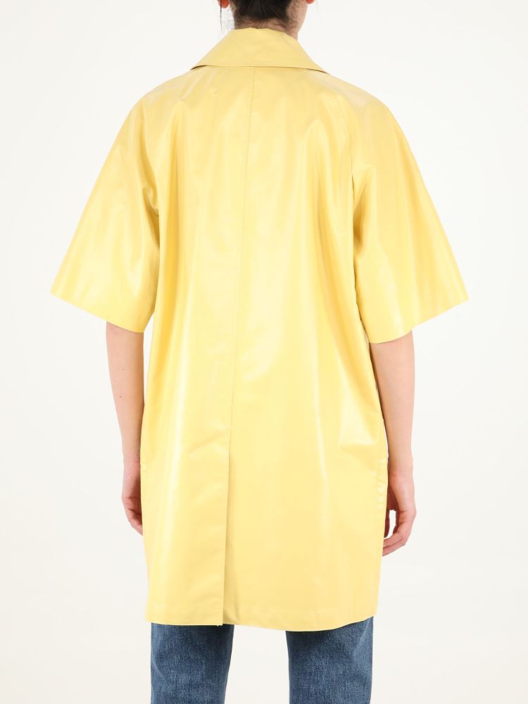 Short-sleeved yellow raincoat with double-breasted closure. It features two side maxi welt pockets and rear slit. The model is 180cm tall and wears size 38.