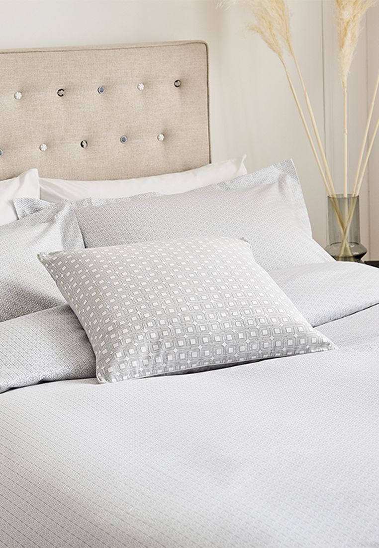 Nikko from Bedeck of Belfast Fine Linens displays a subtle yet sophisticated all over geometric tile print in silky 100% cotton sateen. Available in a choice of silver or linen. Enhance the look further with the coordinating Nikko cushion with repeat interlocking square design embossed with a textured finish and fine cord piping all in 100% cotton sateen also available in silver or linen. Made in Pakistan.