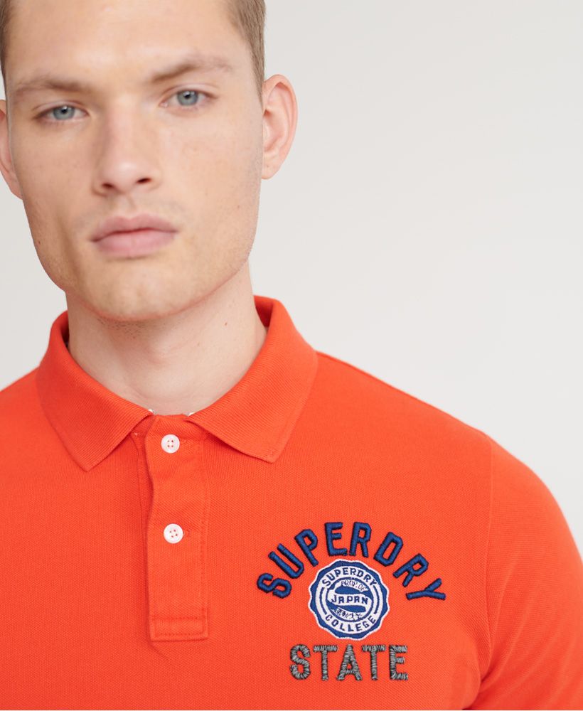 Superdry men's Classic superstate polo shirt. A staple in any wardrobe, this short-sleeved polo features a button fastening at the collar, side splits at the hem and a longer hem at the back. Finished with an embroidered number on one sleeve, and an embroidered Superdry logo on the chest.Slim fit – designed to fit closer to the body for a more tailored lookMade with Organic Cotton - which is grown without the use of artificial chemicals, leading to better soil, 60-90% less water used, and better health for farmers.
