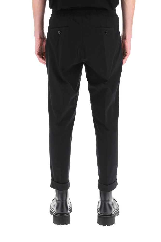 Semi-formal trousers by Neil Barrett, made of extrafine stretch nylon with elasticated waistband and turn-up cuffs. Low rise slim fit, zip fly, side slip pockets, back welt pockets with button. The model is 185 cm tall and wears a size IT 48.
