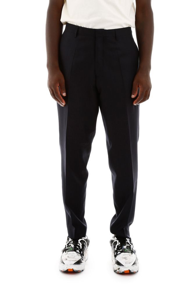 Etudes wool tailoring trousers with pressed pleats. Concealed zip and hook closure, front slanted pockets, back welt pockets. Metallic logo on the front. Model height is 183 cm and he is wearing a size IT 46.