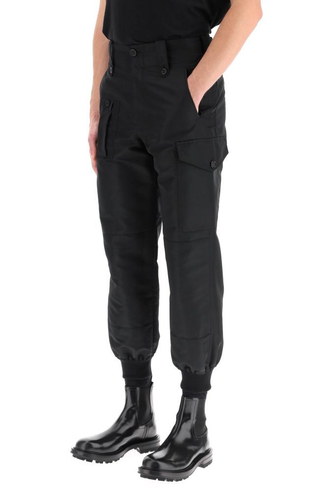 Alexander McQueen military style sports trousers cut from sustainable polyfaille to a straight leg loose fit, detailed with patch pockets with horn buttons on the back. Zip fly and button closure, front welt pockets, one front pocket and a cargo side pocket. Finished with ribbed knit cuffs. The model is 185 cm tall and wears a size IT 46.