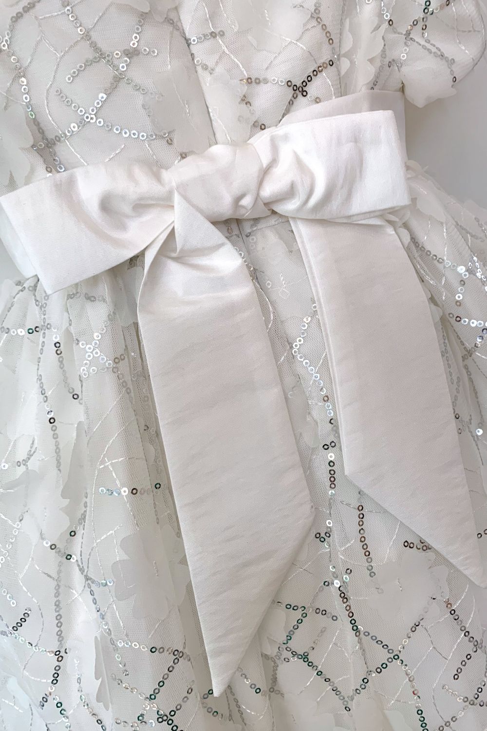 We've ventured out of our comfort zone with reagrds to fabric on this style. We've never used silver sequins on our dresses before now. We love the result in this style TULA, that is perfect for Bridesmaids, Flowergirls, Christenings or Naming Ceremonies.

The fabric is a soft organza with sequins and cut flower shapes all over it. Pretty puffed sleeves and a wide sash belt that ties at the back in a big bow. Truly magical and great for twirling!

We've lined the dress in a fine lawn fabric made of 100% cotton so it's cool and comfortable to wear and a good option for any little girls with sensitive skin.
All our dresses arrive with you on a satin padded hanger to keep the dress in perfect shape, and then protected by one of our Heritage garment keepsake bags.
Outer - 100% polyester excluding sequin trims
lining - 100% cotton
Dry clean or Hand wash only