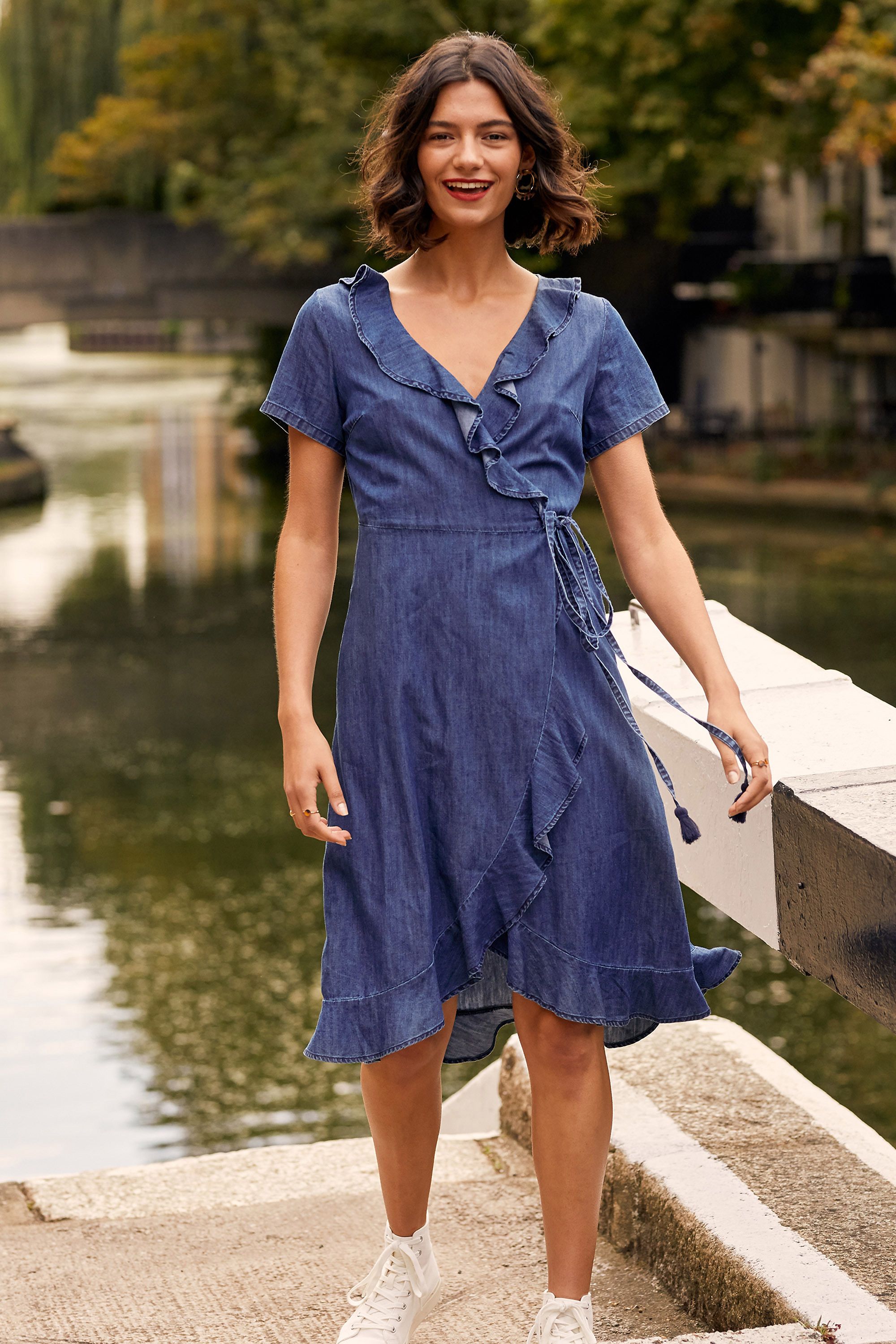 A staple of every wardrobe, this Denim Wrap Dress gives you an effortless choice between smart and casual. Cut in an elegant wrap shape that's super stylish, it's been enhanced with dainty ruffles and a self-tie waist. The cotton chambray gives it a lightweight feel, with a little stretch woven into the fabric for extra movement. Consider trainers and a rucksack for weekend adventures.100% Cotton. Machine Wash At 30. Length is 112cm/40inches