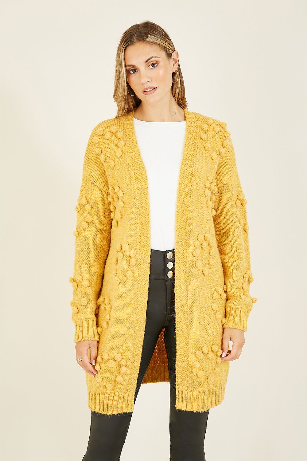 Super soft and in a stunning mustard, this Yumi Mustard Knitted Pom-Pom Heart Long Cardi features statement hand knitted pom poms crafted in heart shaped patterns. A gorgeous, relaxed long cardigan perfect for layering and causal yet cosy weekend wear.