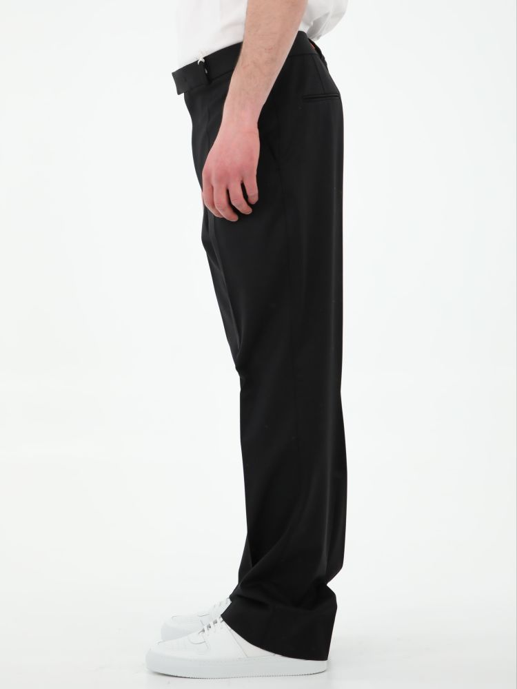 Black wool tailored trousers. It features front concealed closure, two side welt pockets, two rear welt pockets and belt loops. The model is 184cm tall and wears size 50. 