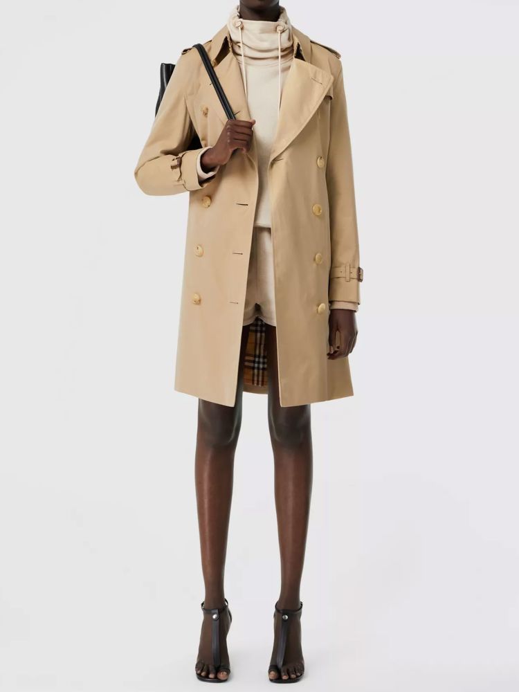 Kensington Heritage trench coat in beige cotton gabardine with double-breasted closure and adjustable belt on waist. It features epaulettes, hook-and-eye collar closure, two side buttoned welt pockets and belted cuffs. The model is 179cm tall and wears size UK 6.