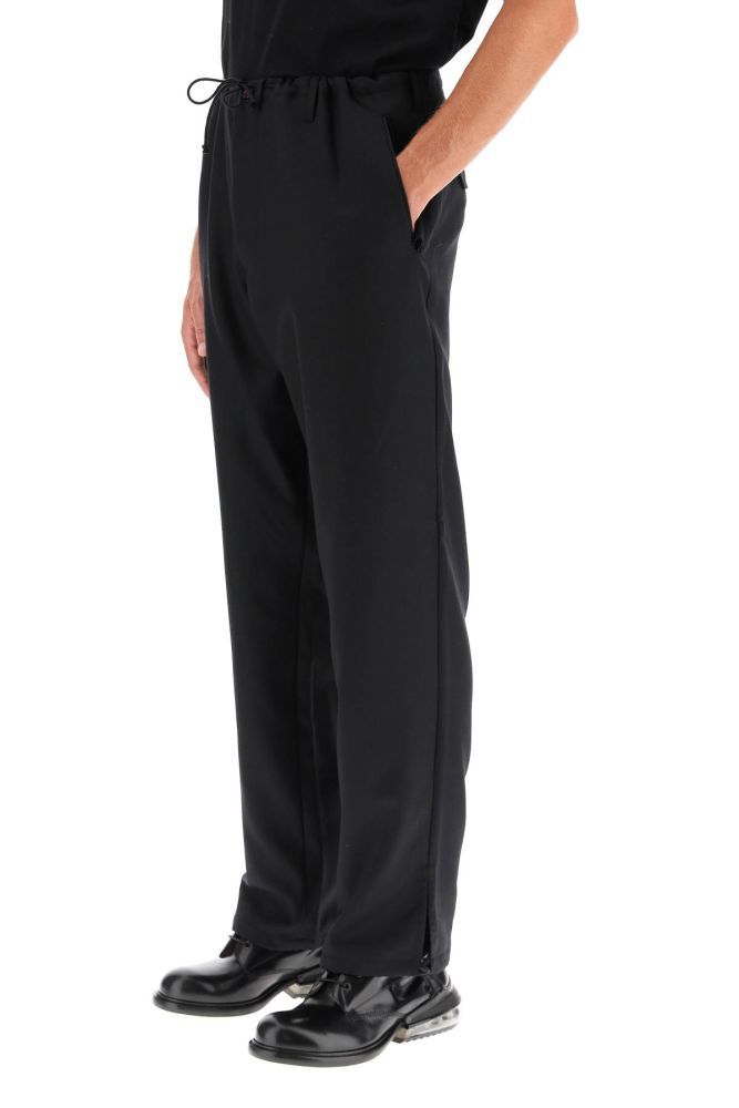 Maison Margiela iconic wide-leg trousers in wool blend gabardine with drawstring waist and cuffs. Side and back pockets lined in striped twill. Detailed with red 