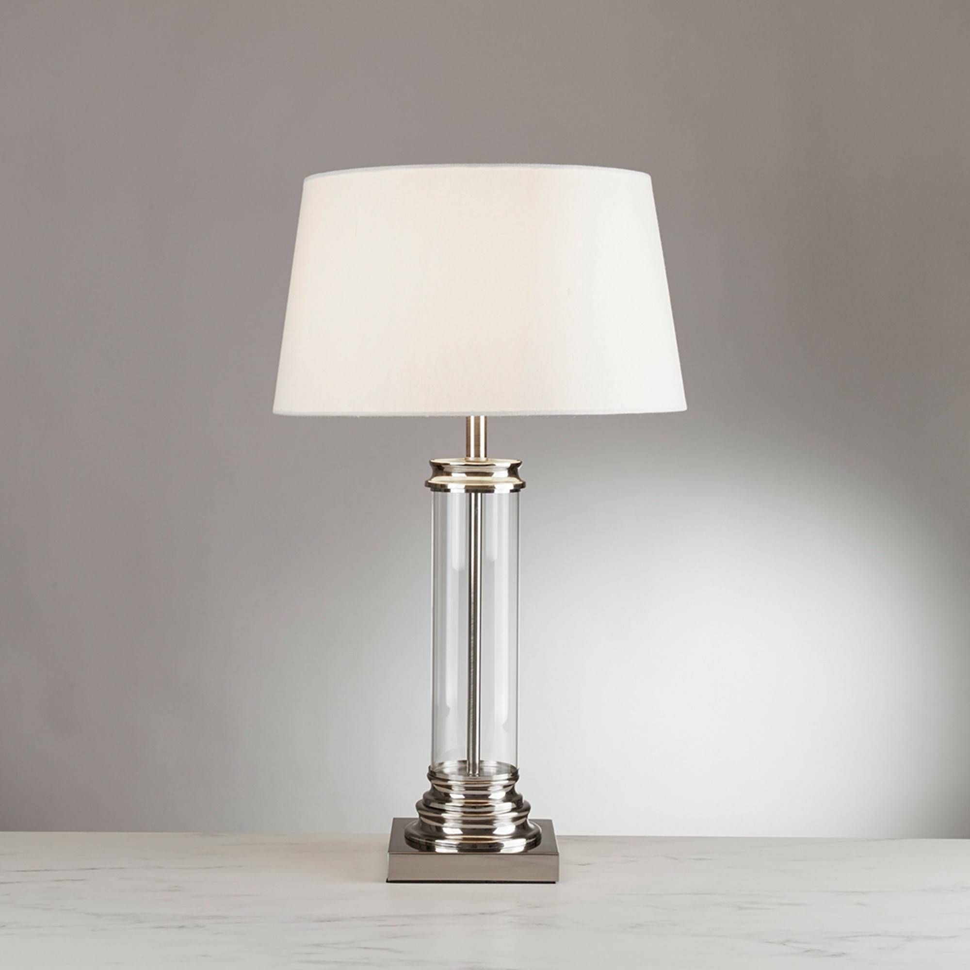 This satin silver vintage inspired table lamp is the perfect addition for a traditional living room or bedroom. The combination of the cream shade, glass column and satin silver base creates a real feeling of sophistication. The clear glass column provides a clean and neat feel which is sure to enhance its surroundings. The fitting has a minimalistic yet elegant look. Class two. Also available in an antique brass finish. Complete with a separate switch on the cable for your convenience. The table lamp is available with a European plug; please contact us for details. | Finish: Satin Silver, Clear | Material: Glass, Fabric, Metal | IP Rating: IP20 | Height (cm): 62 | Diameter (cm): 37 | No. of Lights: 1 | Lamp Type: E27 LED | Wattage (max): 10