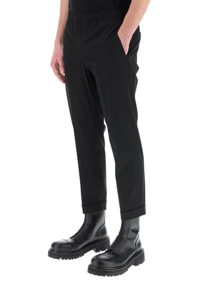 Semi-formal trousers by Neil Barrett, made of extrafine stretch nylon with elasticated waistband and turn-up cuffs. Low rise slim fit, zip fly, side slip pockets, back welt pockets with button. The model is 185 cm tall and wears a size IT 48.