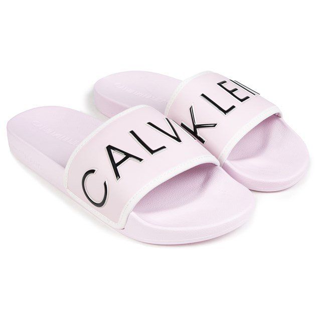 Women's Light Pink Calvin Klein Jeans Slip-on Sandals Designed With A White Edged Wide Toe Strap With Oversized Ck Branding In Black And A Comfy Pu Upper. These Ladies' Pool Style Sliders Have A Contoured Footbed And Flat Rubber Sole With Embossed Calvin Klein Branding.