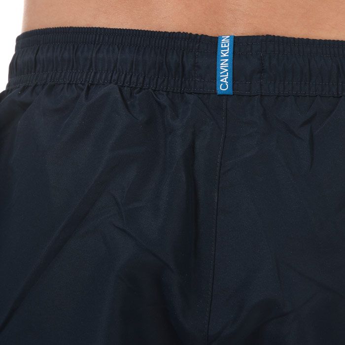 Mens Calvin Klein Short Drawstring Swim Shorts in navy. – Elasticated waist with drawstring. – Mesh lining.  – Slit pockets. – Short length. – Calvin Klein LOGO TAPE trim along sides. – 100% Polyester. Machine washable. – Ref: KM0KM00455CBK