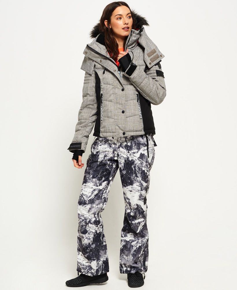 Superdry women’s snow puffer jacket. The snow puffer jacket features a hood with a detachable faux fur trim as well as bungee cord adjusters. This snow jacket benefits from a total of three external zip pockets, including one on the left sleeve, and an internal pocket with a removable cloth for ski goggles. This jacket also has earphone cable routing, removable lining with thumbholes on the cuffs as well as a hook and loop fastening, a removable snow skirt and a bungee cord fastening on the hem. This ski jacket is finished off with Superdry branding on the zips, Superdry logo branding on the cuffs, and two Superdry logo badges on the sleeve. 

Model wears: Small Model height: 5' 10