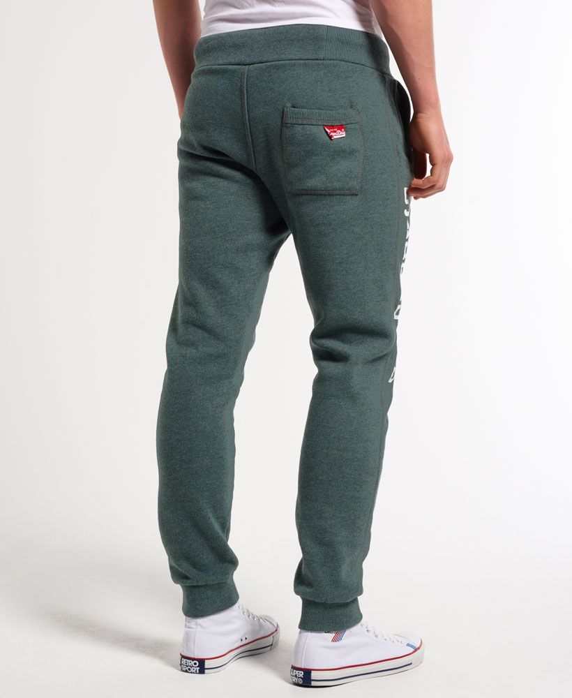 Superdry men's Trackster Slim Joggers. These slimmer fit joggers feature cuffed ankles, cracked print Superdry logo prints on the leg and thigh, three waist pockets and a drawstring waist. The joggers are finished with a Vintage Superdry logo tab on the back pocket and a logo patch on the drawstring. 
Model wears: Medium Model height: 6’ 2” (188cm)