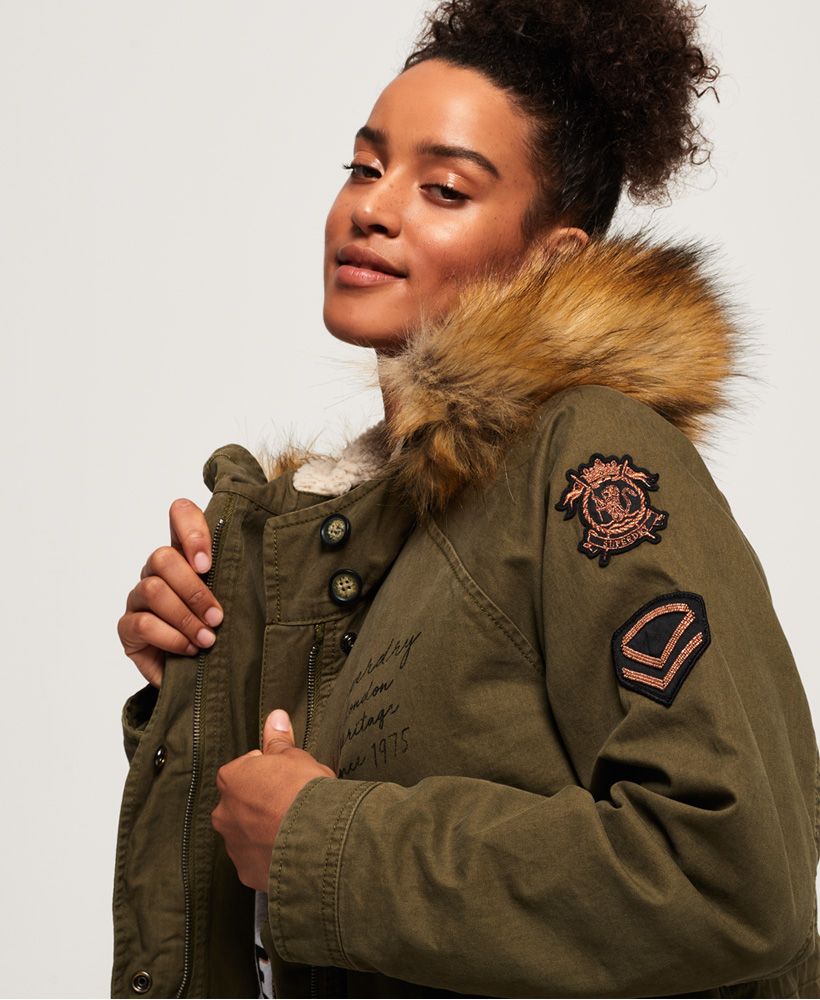 Superdry women's Rookie Heavy Weather tiger parka jacket. The perfect addition to your wardrobe this season, featuring a hood with a removable faux fur trim, a zip and popper fastening, popper fastened cuffs and two front pockets. The Rookie Heavy Weather tiger parka also features a warm fleece lining in the body and hood, a fishtail design and a drawstring adjustable waist for the perfect fit. This jacket is finished with a selection of military inspired badges on the sleeves and Superdry logos on the chest and pocket. Style this jacket with a pair of our skinny jeans and boots for a casual look.