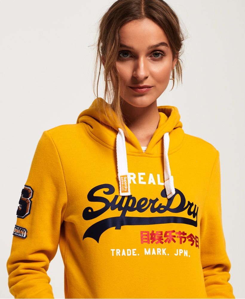 Superdry women's vintage logo bonded satin hoodie. Ideal for a relaxed look, this hoodie is a must-have this season. Featuring a drawstring hood, ribbed cuffs and hem and a front pouch pocket. This hoodie also features a large Superdry logo across the chest in a satin effect, applique badges on the sleeve and is finished with a Superdry logo tab in the side seam.Slim fit