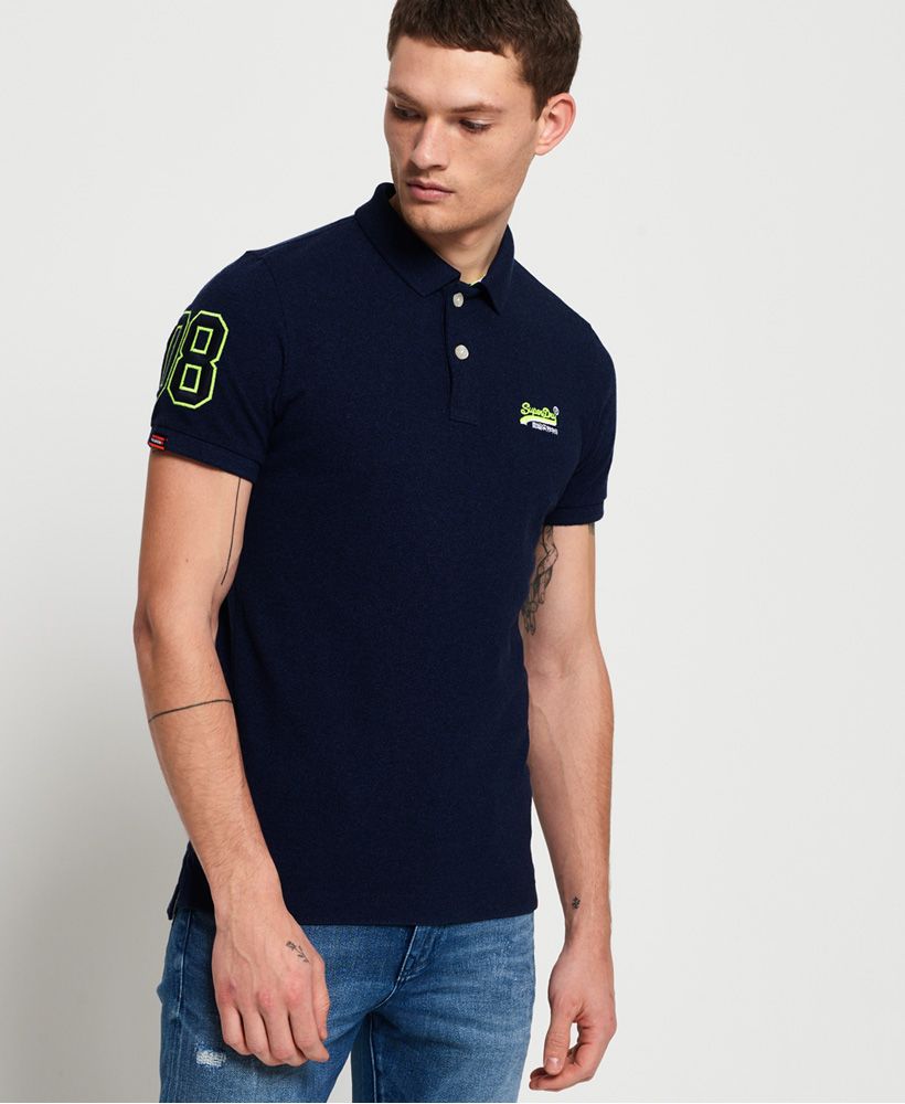 Superdry men's Classic Pique polo shirt. This classic style polo shirt features short sleeves, a two button fastening, reinforced split side seams and an embroidered Superdry logo on the chest. Finished with an embroidered number on one sleeve, a Superdry logo tab on the hem and on one sleeve.Made with Organic Cotton - Made using cotton grown using organic farming methods which minimise water usage and eliminate pesticides, maximising soil health and farmer livelihoods.Slim fit