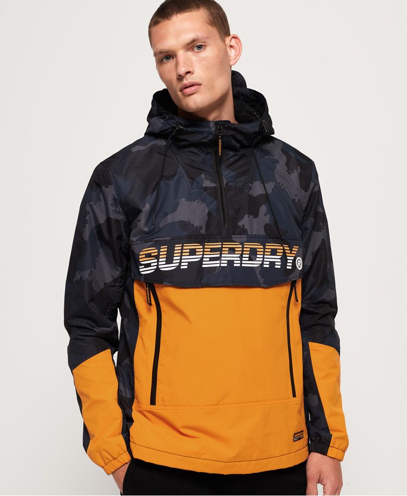 Superdry men's Core overhead cagoule. This winter sports inspired cagoule will not only help to protect you from damp conditions, the fleece lined body will also help keep you warm. With bold branding across the chest flap, underneath a large pouch pocket with twin zip access and a separate zipped pocket can be found. A side zip allows you to put on or remove the cagoule more easily, while a quarter length front zip gives ventilation when required. The integral mesh-lined hood has a bungee cord adjuster along with a small peak. The cagoule is finished with a small logo patch above the hem and branded zip pullers throughout.