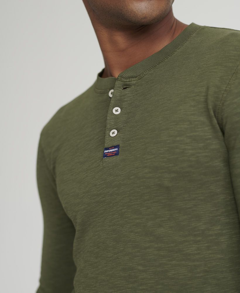 Superdry men's Legacy long sleeve Henley top. A long sleeved top featuring Henley collar with button fastening, and ribbed cuffs. Finished with a Superdry logo patch on the placket, this top is ideal for pairing with jeans or chinos for a smart casual look.