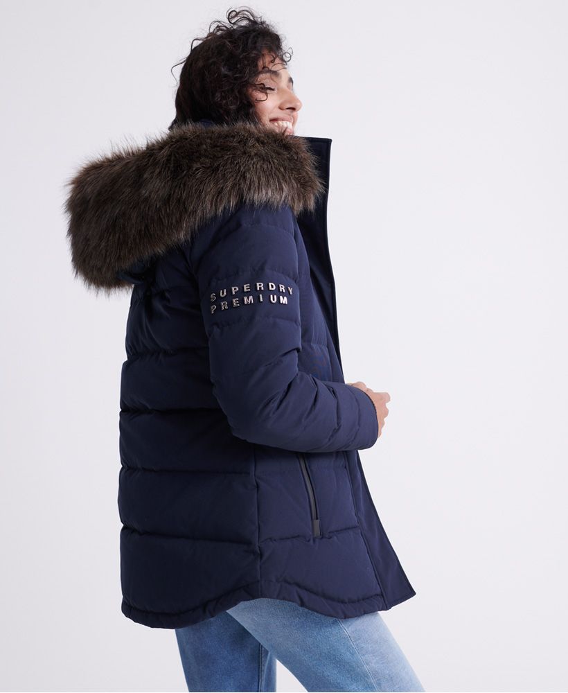 Superdry women's Premium down trophy jacket. Stay warm this season with this duck down jacket featuring a 90/10 duck and feather fill, a zip a button fastening, a bungee cord adjustable hood with adjustable faux fur trim, bungee cord adjustable hem, and ribbed cuffs. This warm and cozy jacket also features two large zip fastened pockets, an inner pockets to store your valuables, a bungee cord adjustable waist, and ventilation under the arms. Finished with a Superdry Premium embellishment on one sleeve, and a Superdry logo patch on the other.Superdry is certified by the Responsible Down Standard to confirm that our down filled products are sourced to ensure animal welfare.