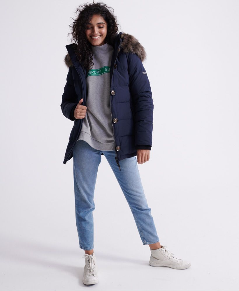 Superdry women's Premium down trophy jacket. Stay warm this season with this duck down jacket featuring a 90/10 duck and feather fill, a zip a button fastening, a bungee cord adjustable hood with adjustable faux fur trim, bungee cord adjustable hem, and ribbed cuffs. This warm and cozy jacket also features two large zip fastened pockets, an inner pockets to store your valuables, a bungee cord adjustable waist, and ventilation under the arms. Finished with a Superdry Premium embellishment on one sleeve, and a Superdry logo patch on the other.Superdry is certified by the Responsible Down Standard to confirm that our down filled products are sourced to ensure animal welfare.