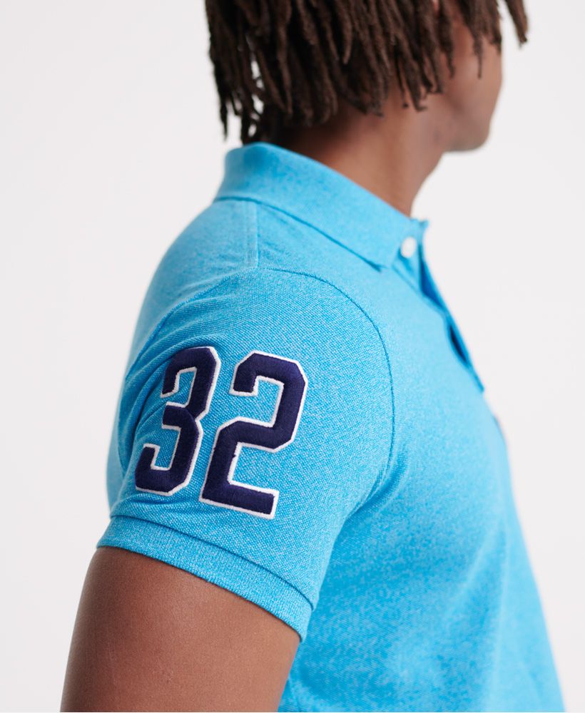 Superdry men's Classic superstate polo shirt. A staple in any wardrobe, this short sleeved polo features a button fastening at the collar, side splits at the hem, and a longer hem at the back. Finished with an embroidered number on one sleeve, and an embroidered Superdry logo on the chest.Made with Organic Cotton - Grown using only organic inputs and no artificial chemicals, which leads to improved soil condition, stronger biodiversity and better health among the cotton growers and uses between 60-90% less water to grow. By 2030, all Superdry Cotton will be Organic.Slim fit
