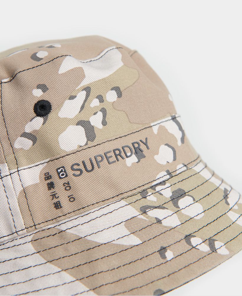 Superdry women's Reversible bucket hat. Go from one look to anther with this reversible bucket hat featuring, stitched eyelet detailling and a choice of two patterns. Finished with a Printed Superdry logo on one side and a Superdry logo tab on the other.