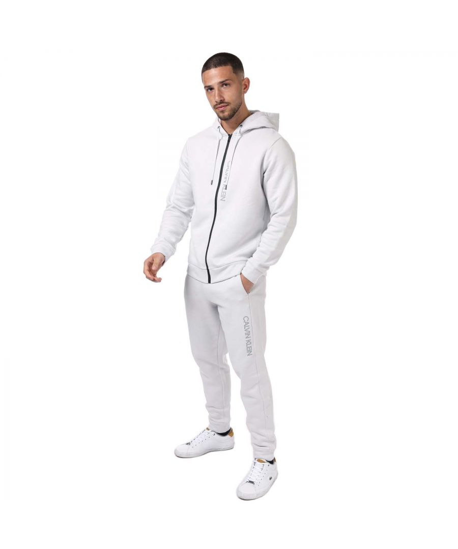 Mens Calvin Klein Performance Essentials Tracksuit in grey.- Hoodie:- Hood with drawcords.- Long sleeves.- Side slip pockets.- Zip fastening.- Ribbed trims.- Lettering logo.- Shell: 87% Cotton  13% Polyester. - Bottoms:- Elasticated waist with drawstring.- Slide slip pockets.- Rib-knit cuffs.- Calvin Klein lettering logo on the upper leg.- Regular fit.- Shell: 87% Cotton  13% Polyester. - Ref: 00GMF1J418020