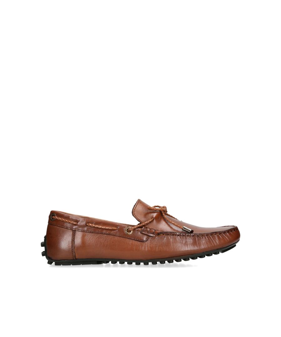 The Felix is a slip on loafer crafted in a tan leather. There is a brown braided strap pulling through the upper which creates a bow at the vamp.