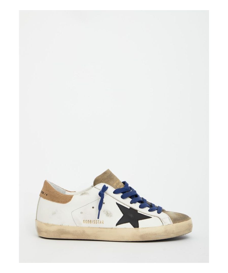 Super-Star sneakers in white leather with black leather side star and grey suede details. They feature blue lace-up closure, brown heel with Golden Goose logo, side GGDB/SSTAR lettering, round toe and rubber sole.