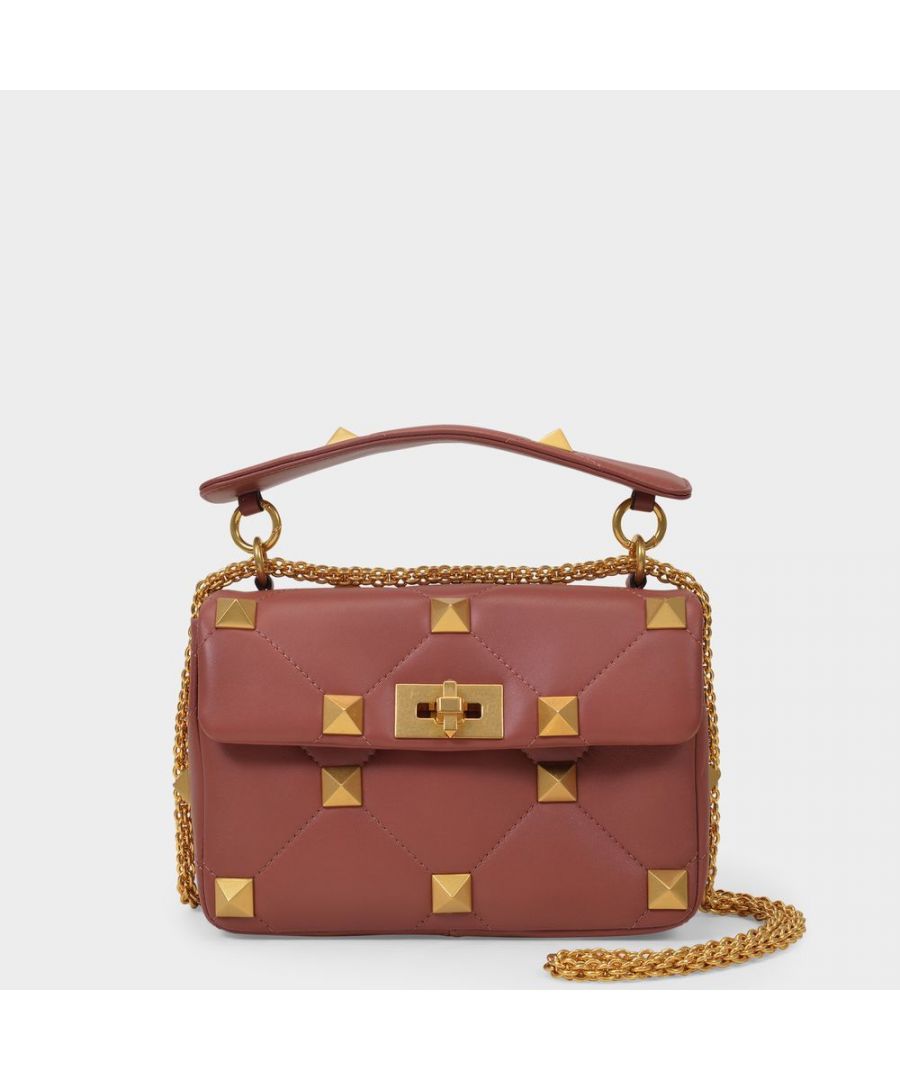 We love the Roman Stud from Valentino for its quilted design, oversize handle and signature studs. A chic piece that doesn't shy away from its punk influences. Shoulder strap : 55 cm. Worn two ways - one strap and one chain. Material: smooth lambskin. Lining: leather. Colour : Marron - Pvg Ginger Bread. Closure : pivoting clasp. Interior : one zipped pocket, one flat pocket.