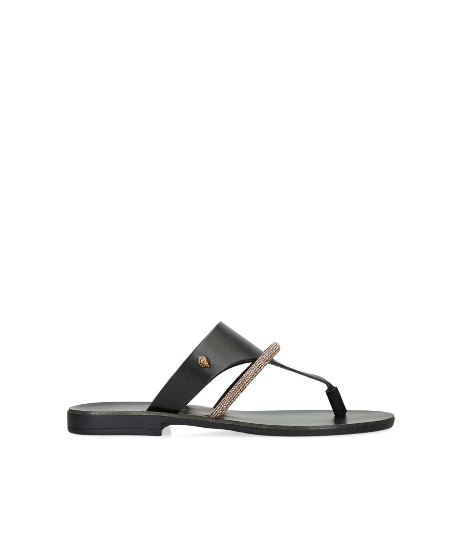 The KGL Strand is a black leather toe post sandal. There is a smaller, crystal embellished strap across the foot. The antiqued brass Eagle head sits on the outer side.