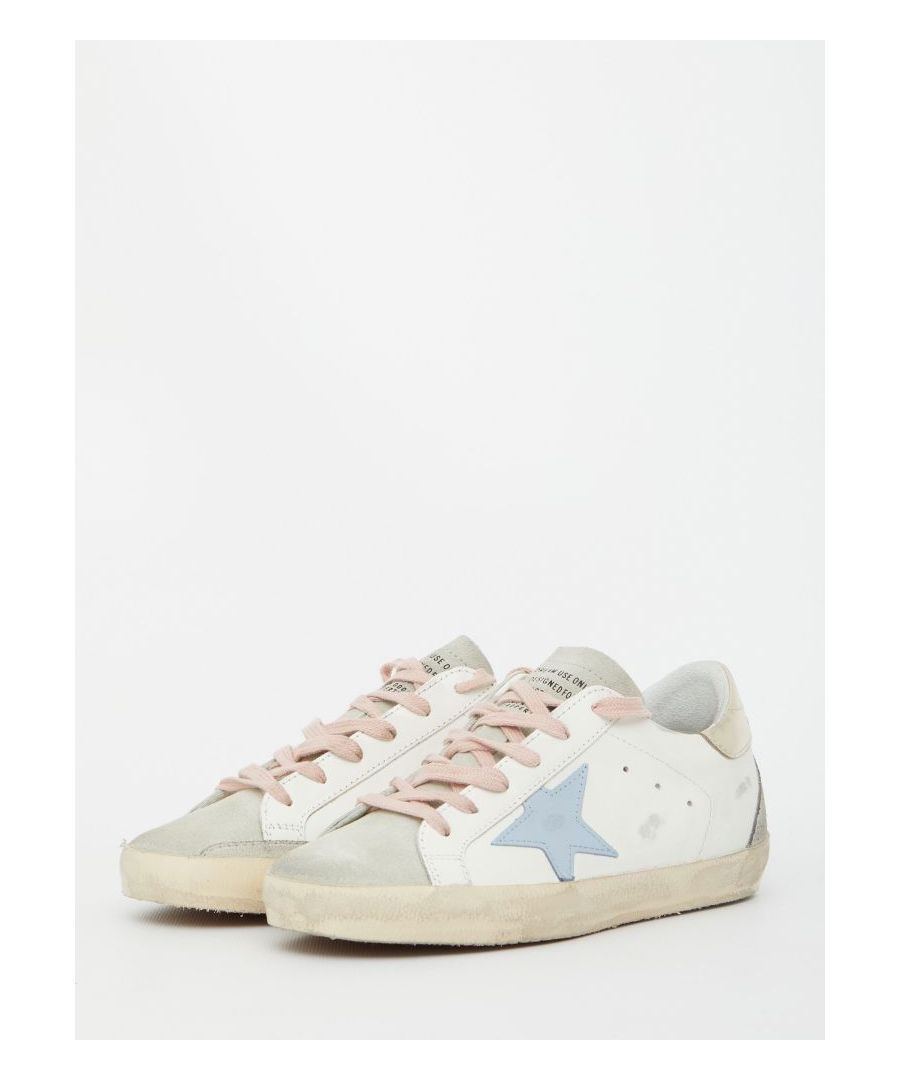 Super-Star sneakers in white leather with Golden Goose side star in light-blue leather and grey suede details. They feature pink lace-up closure, silver-tone heel with Golden Goose logo, metal GGDB side lettering, round toe and vintage effect. Rubber sole.