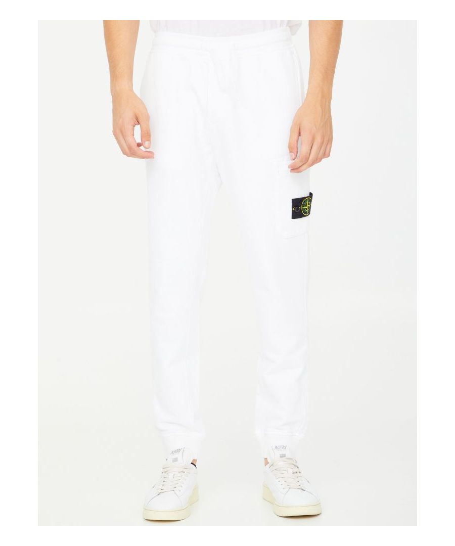 White cotton fleece pants. It features elasticated waist with drawstring, two side welt pockets, a patch pocket on left sleeve with Stone Island logo patch and a rear welt pocket. Elasticated ankle cuffs. The model is 190cm tall and wears size L.