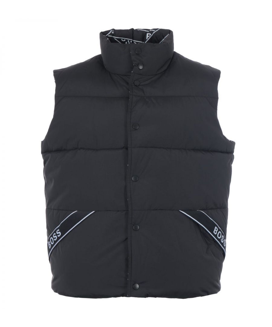 Offering two looks in one this reversible gilet from BOSS is a stylish layering piece to add to your new season wardrobe. Crafted from a technical poplin and padded with sustainably sourced recycled fibres providing warmth and comfort. One side sports an all over tape effect print whilst the other is a solid colour with subtle logo-tape trims. Featuring a stand up collar, snap button closure and snap button pockets fitted to each side. Finished with subtle BOSS branding to the hardwear for a signature touch.Regular Fit, Technical Nylon Poplin, Recycled Polyester Padding, Stand Up Collar, Snap Button Closure, Four Snap Button Pockets, Reversible Design, BOSS Branding. Style & Fit:Regular Fit, Fits True to Size. Composition & Care:Shell: 100% Polyamide, Fill: 100% Recycled Polyester, Professional Wet Clean.
