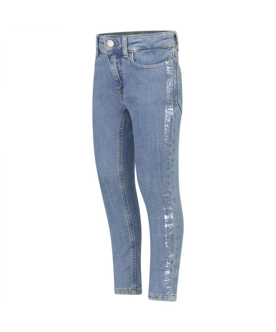 Girls blue denim jeans from Calvin Klein. Featuring signature button waistband with belt loops, zip-fly, five pocket styling with metal rivets, embroidered 'CK' on the coin pocket, shimmery logo trim along the seams, a stitched branded shimmery leath