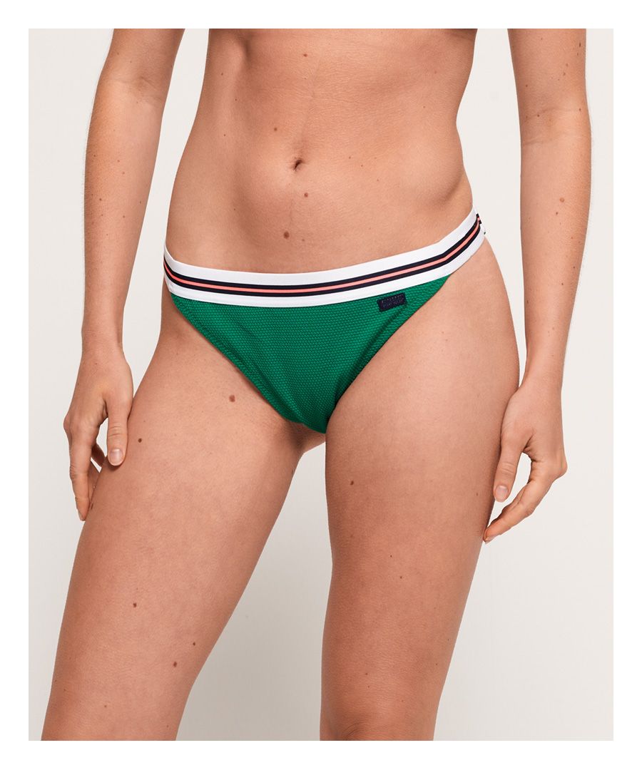 Superdry 90's Retro Cheeky-bikinibroekje. Dit brutale bikinibroekje heeft een elastische tailleband met gestreepte details en is afgewerkt met een metalen Superdry-logobadge op de voorkant.Bijpassend topje apart verkrijgbaar.Om hygiënische redenen kan badmode uitsluitend omgeruild of geretourneerd worden als de hygiënestrip nog intact is. Dit doet geen afbreuk aan je wettelijke rechten.
