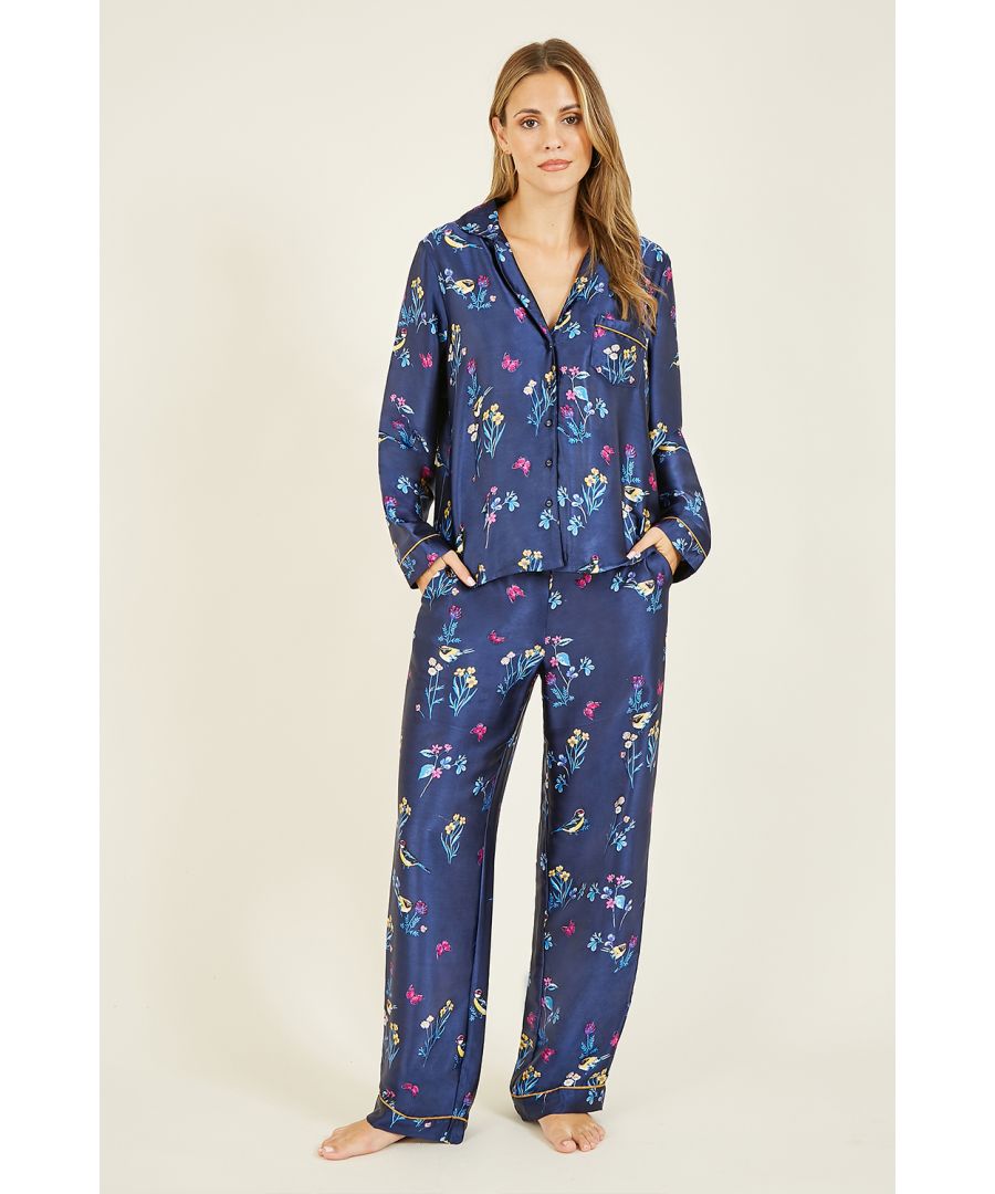 Nachtkleding, maar dan luxe. Deze marineblauwe satijnen pyjama met vogelprint is versierd met een sierlijk bloemen- en vogelpatroon. Het topje heeft een volledige knoopsluiting, een kraag en lange mouwen en één zak. De 3-delige set bestaat uit een loose-fit broek en een satijnen pyjamatas.