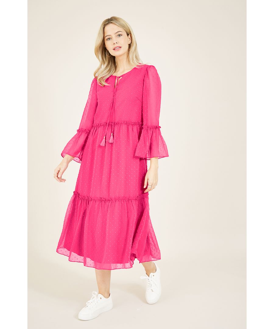 Deze smock midi-jurk met dobbystippen vloeit in een elegante, gelaagde vorm onder de knie en is er een om ruimte voor te maken in je garderobe. Gemaakt in een relaxte vorm die super flatteus is, met lange, wijd uitlopende mouwen en een ronde hals versierd met een band met kwastjes. De gelaagde lichtgewicht stof voegt veel flow toe, aangevuld met de subtiele ruches die de lagen versieren. Til je look naar het volgende niveau met een paar hakken voor leukere evenementen of houd alles casual met witte sneakers en een denim jas.